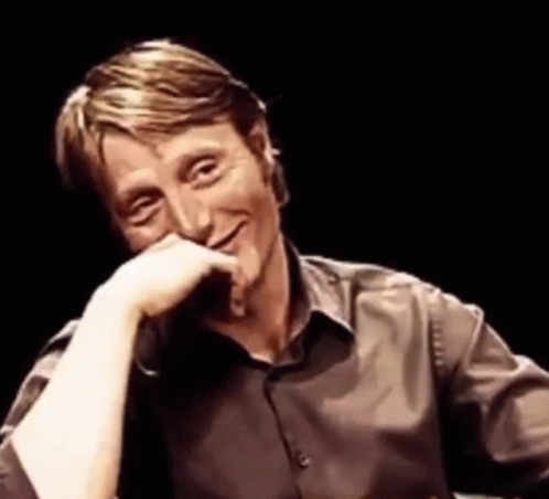 A Man In A Brown Shirt Is Smiling With His Hand On His Face . GIF