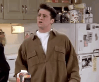 A Man In A Brown Shirt Is Standing In Front Of A Refrigerator Holding A Bottle Of Milk . GIF