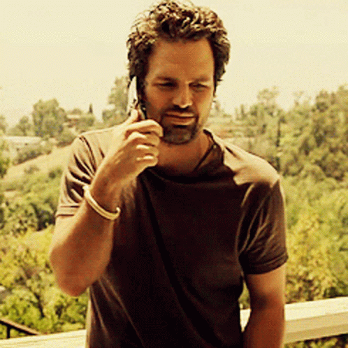 A Man In A Brown Shirt Is Talking On His Cell Phone GIF