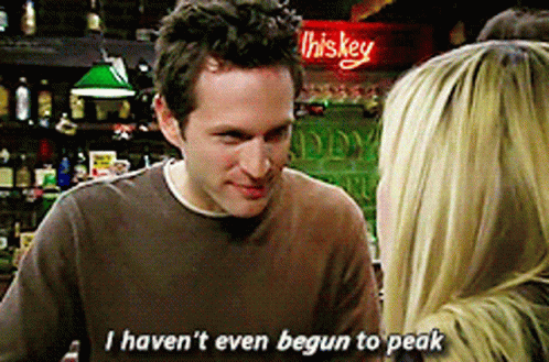 A Man In A Brown Shirt Is Talking To A Woman In Front Of A Sign That Says Whiskey GIF