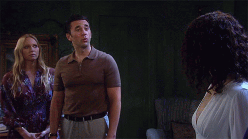 A Man In A Brown Shirt Stands Next To A Woman In A White Dress GIF