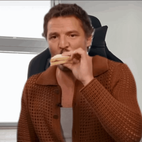 A Man In A Brown Sweater Is Eating A Piece Of Bread GIF
