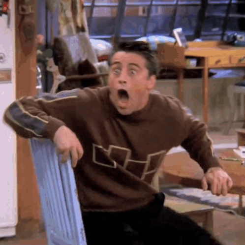 A Man In A Brown Sweater Is Sitting In A Chair With His Mouth Open . GIF