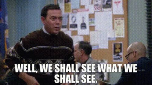 A Man In A Brown Sweater Is Standing In Front Of A Bulletin Board And Says Well We Shall See What We Shall See GIF