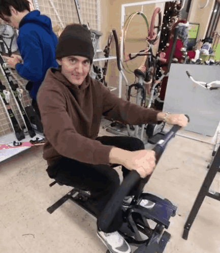 A Man In A Brown Sweatshirt Is Sitting On A Machine GIF
