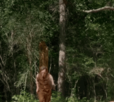 A Man In A Brown Vest And Pants Is Walking Through A Forest GIF