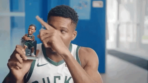 A Man In A Bucks Jersey Is Holding A Figurine Of A Basketball Player And Pointing At It . GIF