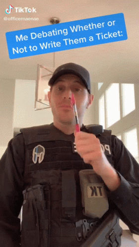 A Man In A Bullet Proof Vest Is Holding A Red Pen In His Mouth With A Tiktok Sticker Above Him GIF