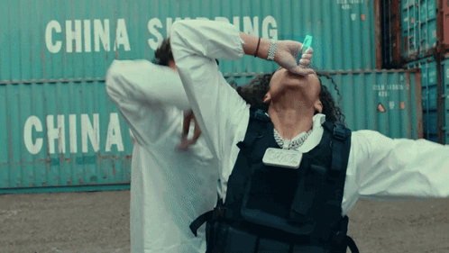 A Man In A Bullet Proof Vest Is Standing In Front Of A China Shipping Container GIF