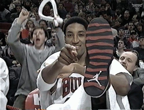 A Man In A Bulls Jersey Holds Up His Shoe In Front Of A Crowd GIF