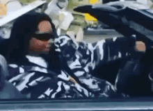 A Man In A Camouflage Jacket Is Driving A Car . GIF