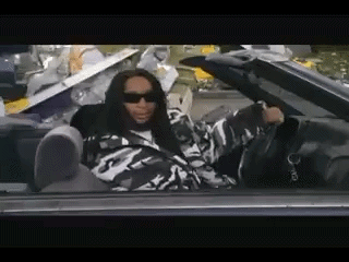 A Man In A Camouflage Jacket Is Sitting In A Car With His Feet Up . GIF