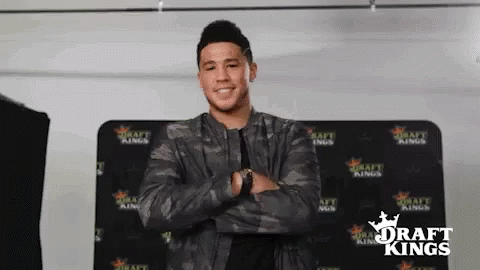 A Man In A Camouflage Jacket Is Standing With His Arms Crossed In Front Of A Draft Kings Sign . GIF