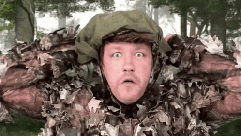 A Man In A Camouflage Outfit Is Making A Surprised Face . GIF