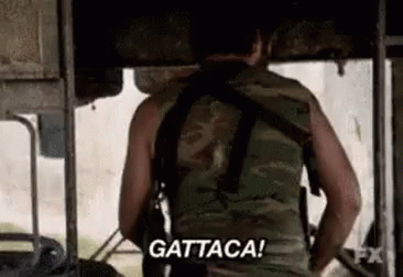 A Man In A Camouflage Vest Is Holding A Gun And Saying `` Gattaca '' . GIF