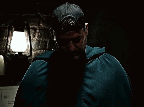 A Man In A Cape Covering His Face With His Hands In A Dark Room GIF