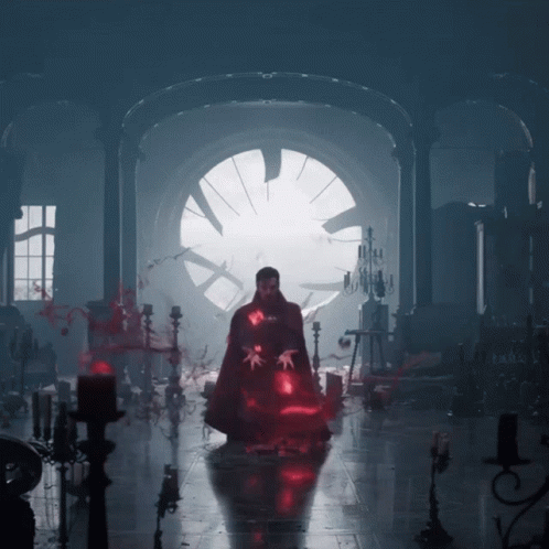 A Man In A Cape Is Standing In A Dark Room With Candles GIF