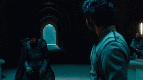 A Man In A Cape Stands In Front Of A Man With A Headless Figure GIF