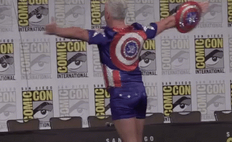 A Man In A Captain America Costume Is Standing In Front Of A Comic Con Sign GIF