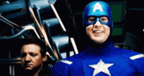 A Man In A Captain America Costume Stands Next To Another Man GIF