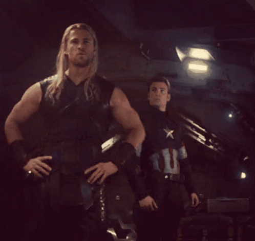 A Man In A Captain America Uniform Stands Next To A Man In A Leather Vest GIF