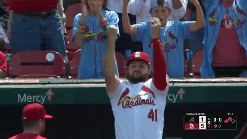 A Man In A Cardinals Jersey Stands In Front Of A Mercy Sign GIF
