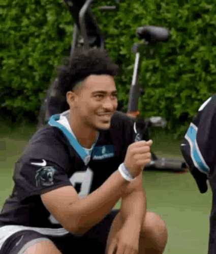 a man in a carolina panthers jersey is sitting on the ground and smiling .