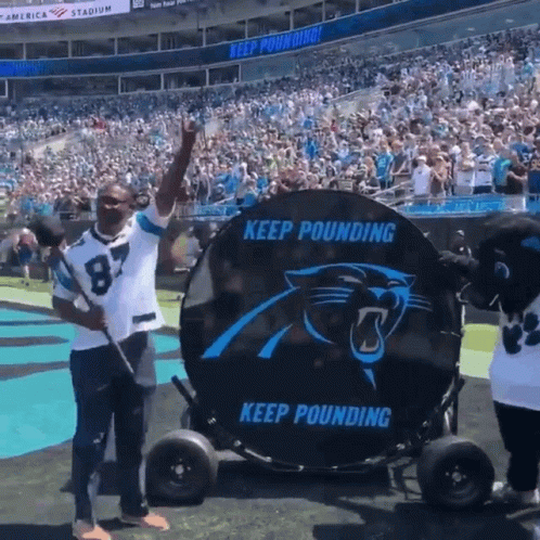 A Man In A Carolina Panthers Jersey Is Standing In Front Of A Large Keep Pounding Sign GIF