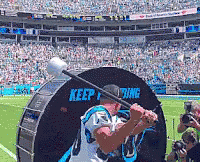 A Man In A Carolina Panthers Jersey Is Swinging A Bat In Front Of A Keep Fighting Sign GIF