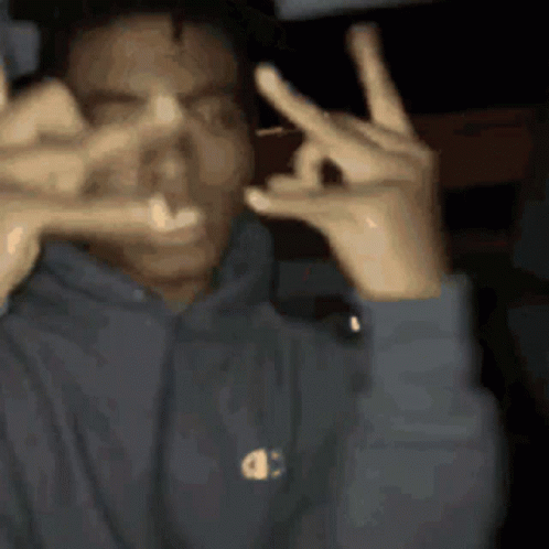 A Man In A Champion Hoodie Is Making A Peace Sign GIF