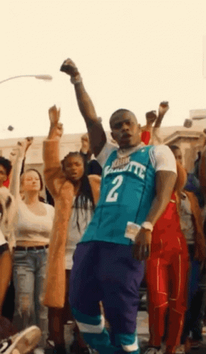 A Man In A Charlotte Hornets Jersey Is Standing In Front Of A Crowd Of People . GIF