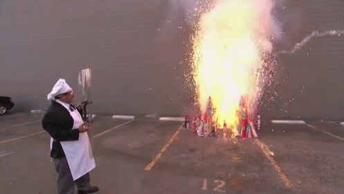 A Man In A Chef 'S Hat And Apron Stands In Front Of A Large Fire GIF