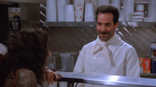 A Man In A Chef 'S Uniform Is Talking To A Woman Behind A Counter GIF