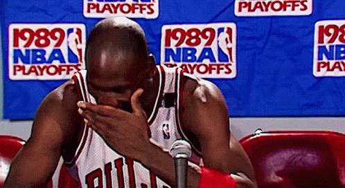 A Man In A Chicago Bulls Jersey Covering His Face In Front Of A Nba Playoffs Banner GIF