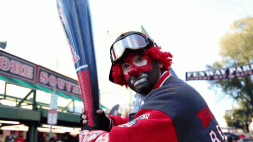 A Man In A Clown Costume Is Holding A Bat In Front Of A Sign That Says Boston South GIF