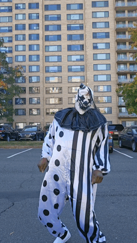 A Man In A Clown Costume Is Standing In A Parking Lot In Front Of A Tall Building GIF