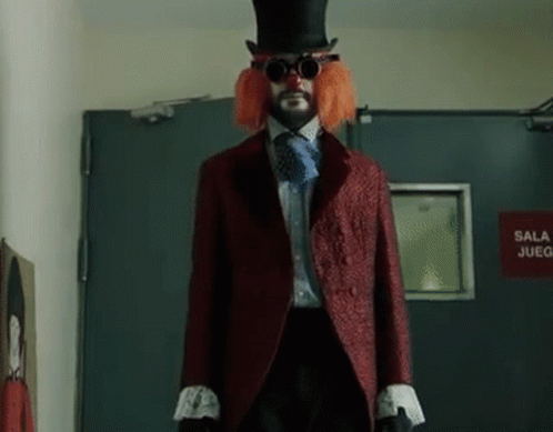A Man In A Clown Costume Is Standing In Front Of A Red Sign That Says Sala Juego GIF
