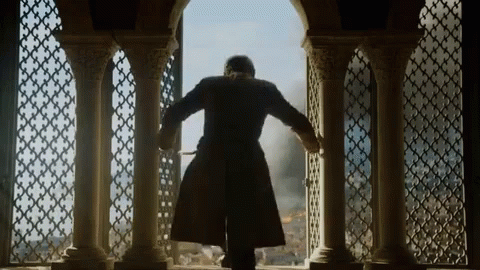 A Man In A Coat Is Standing In Front Of A Window With Columns GIF