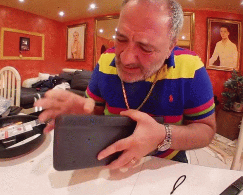 A Man In A Colorful Polo Shirt Is Holding A Black Object GIF