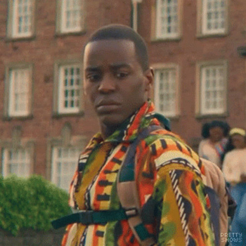 A Man In A Colorful Shirt And Backpack Is Standing In Front Of A Brick Building . GIF
