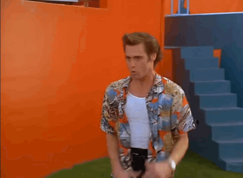A Man In A Colorful Shirt And Black Pants Is Dancing In Front Of An Orange Wall And Stairs . GIF