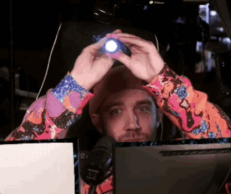 A Man In A Colorful Shirt Is Holding A Flashlight In Front Of His Head GIF