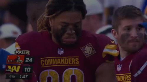 A Man In A Commanders Jersey Is Being Helped By Another Man GIF