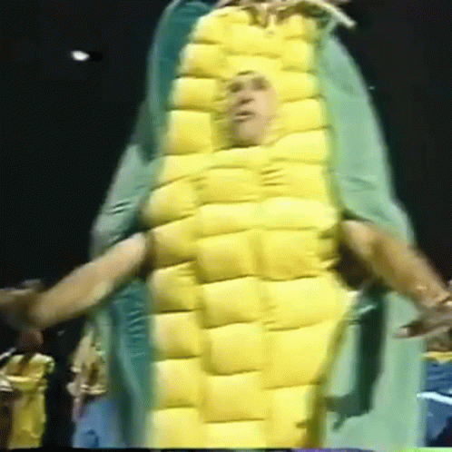 A Man In A Corn On The Cob Costume Is Being Held By Another Man GIF