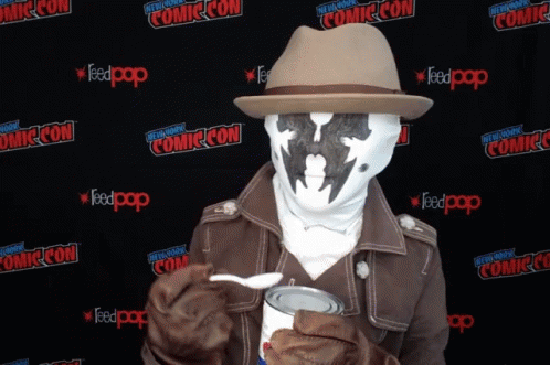 A Man In A Costume Is Holding A Can Of Food In Front Of A Wall That Says Comic Con On It GIF