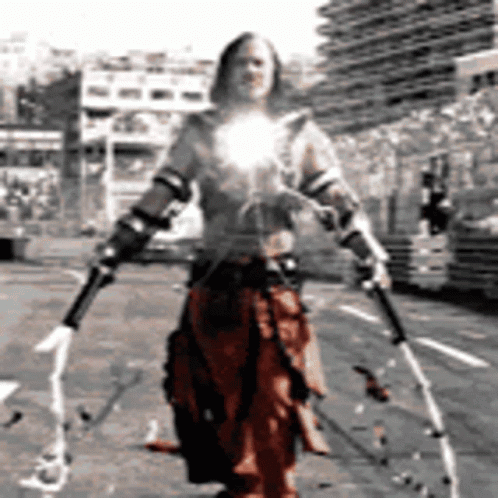 A Man In A Costume Is Holding Two Swords In Front Of A Building GIF