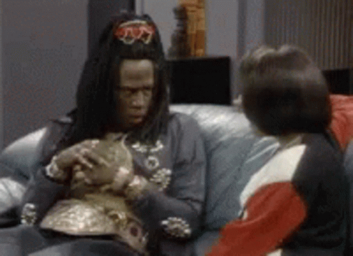 A Man In A Costume Is Sitting On A Couch Holding A Cat . GIF