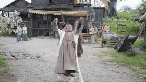 A Man In A Costume Is Standing On A Dirt Road Holding A Sword In His Hands . GIF