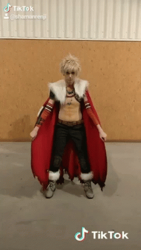 a man in a costume with a red cape is standing in front of a wooden wall .