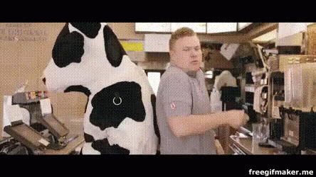 A Man In A Cow Costume Is Standing Next To A Cow Mascot In A Restaurant . GIF